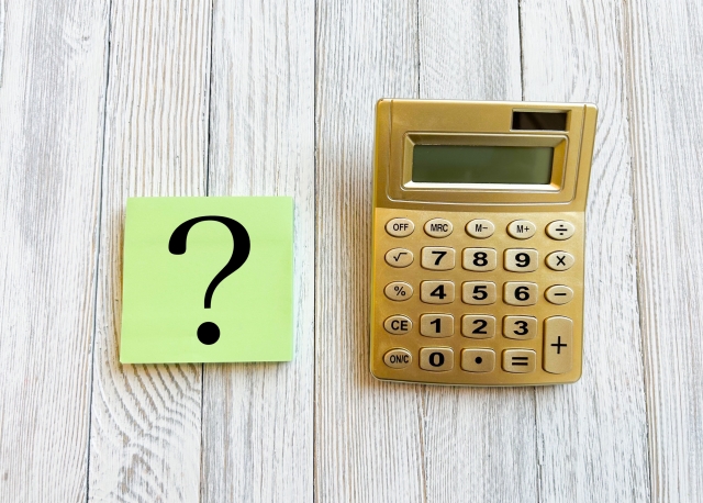 金色の電卓 クエスチョンマーク 白い木目の床