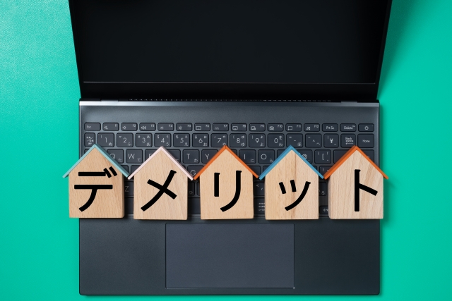 家型プレートにデメリットの文字 黒いノートパソコン、