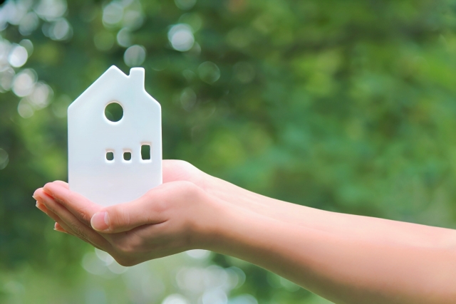 置物の家を持つ手 白い家の置物 グリーンの背景